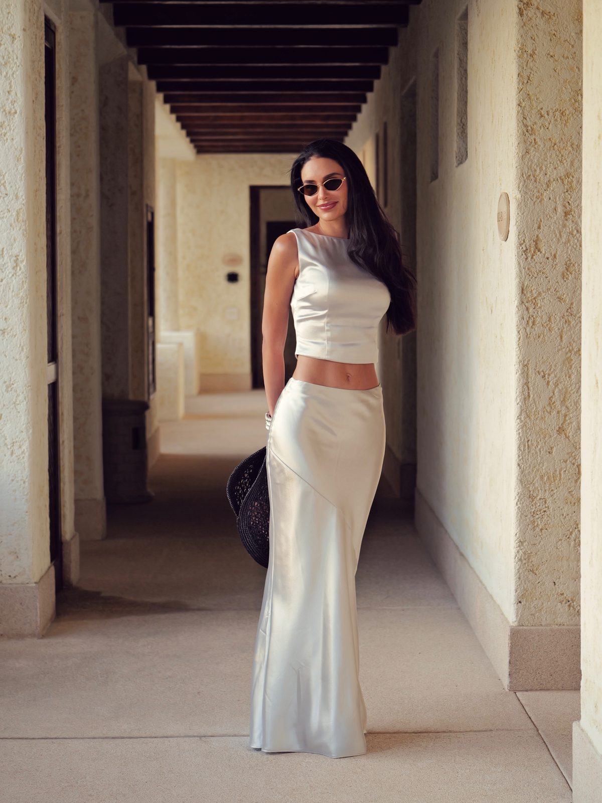 Jamillette in a cream top and long satin skirt in a pale stone corridor with timber beams