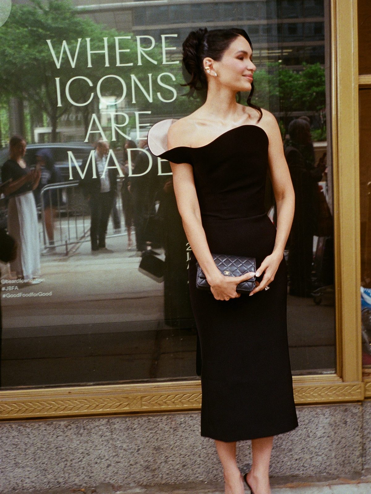 Jamillette in a black off-shoulder dress beside a window that reads Where Icons Are Made