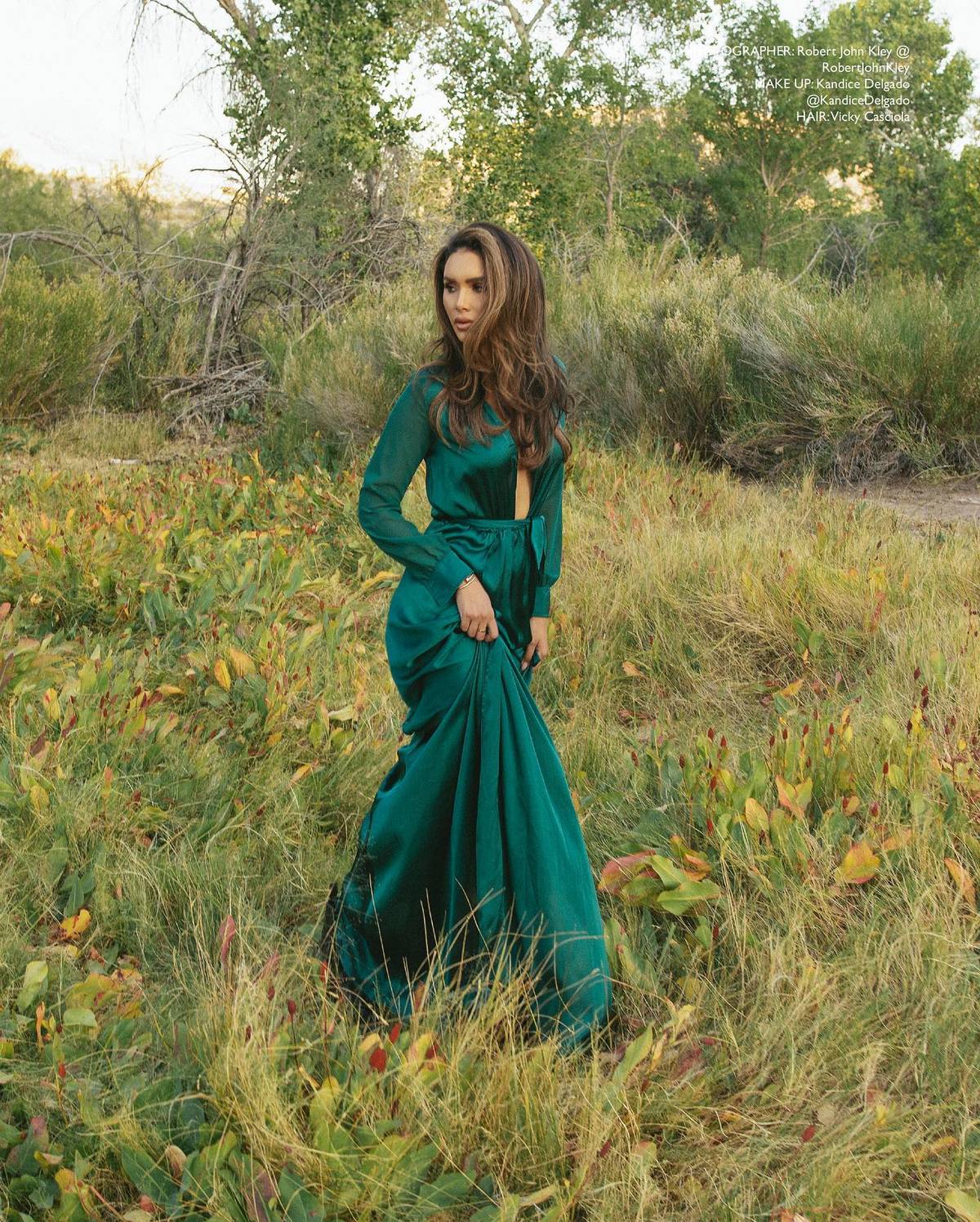 Jamillette in an emerald green satin gown, standing in a field of tall grass