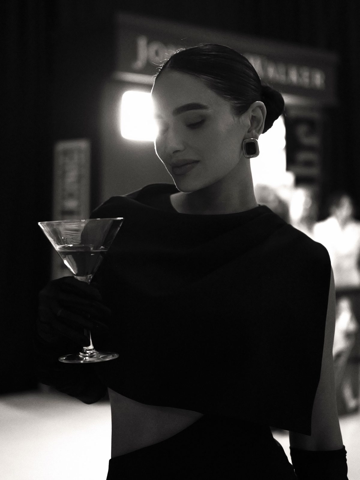 Black and white portrait of Jamillette in a black draped top, holding a martini glass