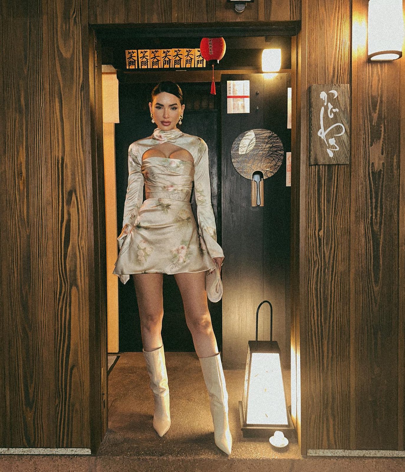 Jamillette in a silver jacquard mini dress and white boots at a wooden entrance with paper lanterns