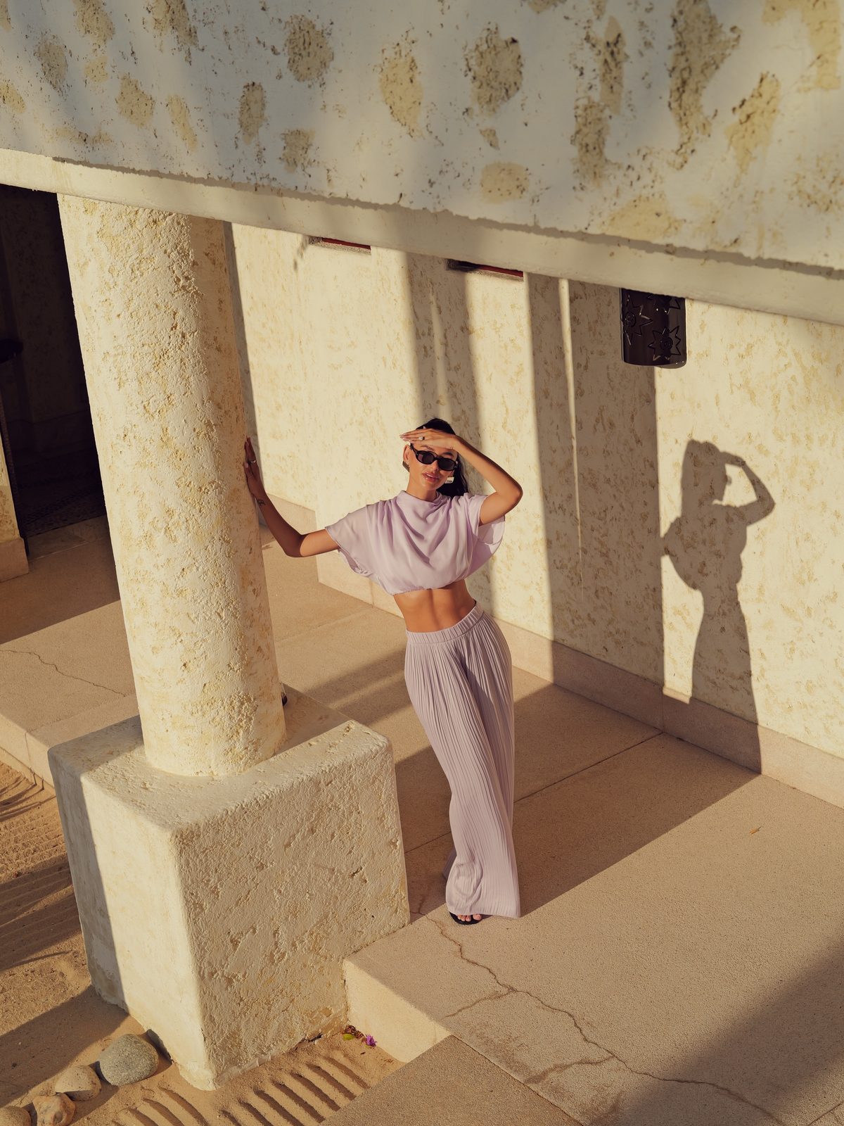 Jamillette in a mauve pleated two-piece between pale stone columns, shading her eyes