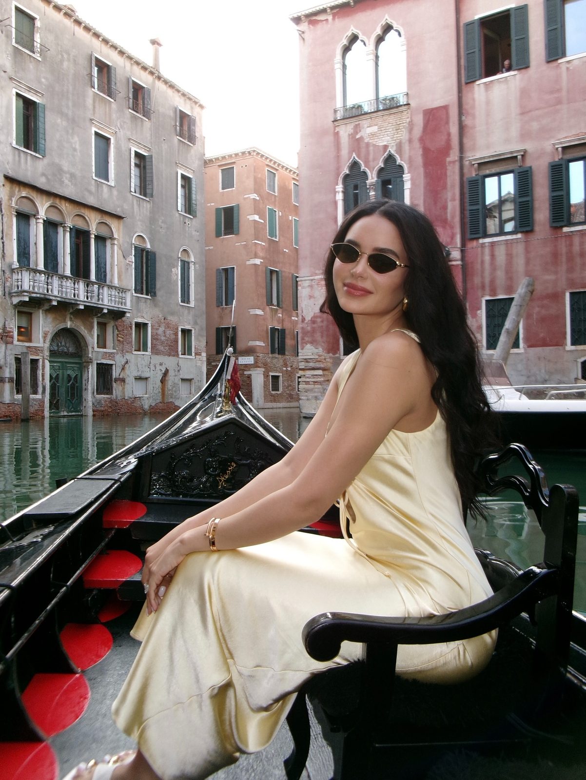 Jamillette in a pale yellow satin dress, seated in a gondola on a Venetian canal